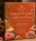 Gratitude Affirmation Card Deck box with a terracotta orange cover, decorated with a pink lotus flower, candle, crystals, and knitted fabric. The box features the text 'Gratitude Heals' and 'Gratitude Affirmation Card Deck' in white and gold lettering.
