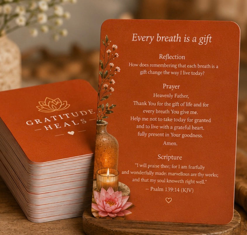 A stack of terracotta-colored mindfulness cards labeled 'Every breath is a gift' with printed reflection, prayer, and scripture text, displayed on a wooden surface beside a small lit candle and pink flower.